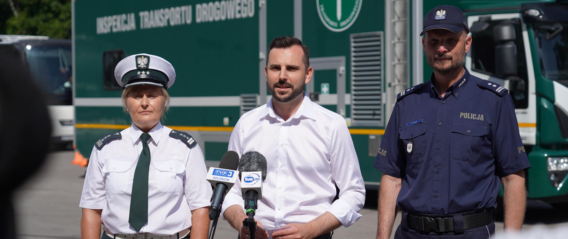 w środku przed mikrofonami stacji telewizyjnych wicewojewoda, po lewej wojewódzka inspektor transportu drogowego, po prawej zastępca komendanta wojewódzkiego policji. W tle samochód Inspekcji Transportu Drogowego.