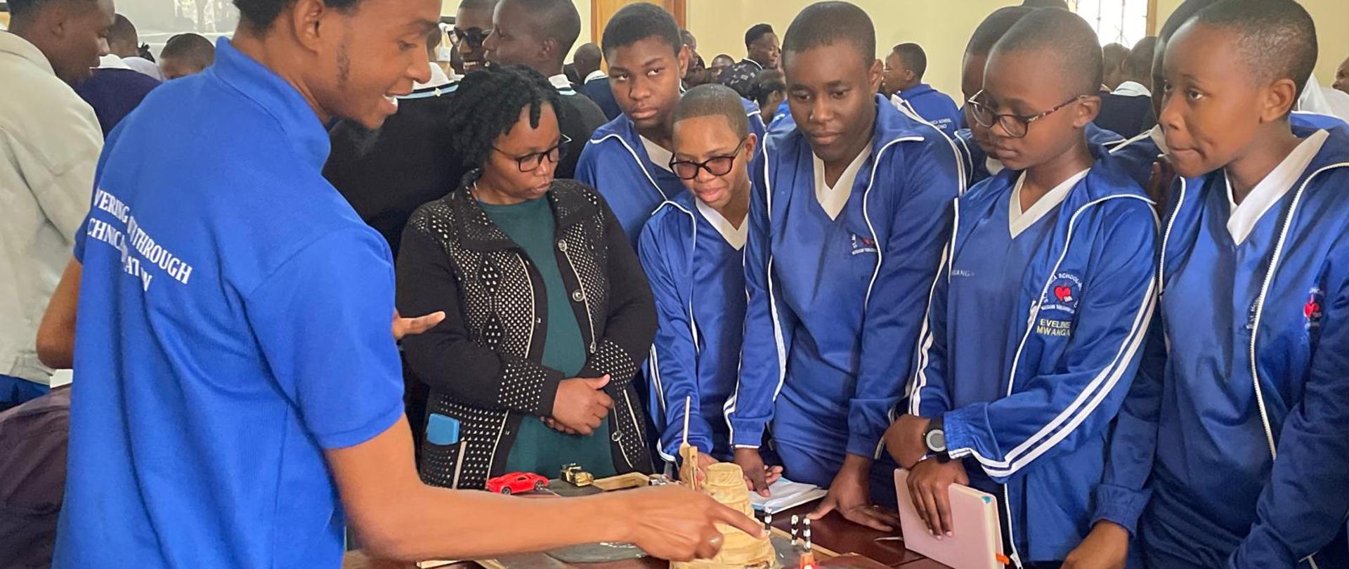 Makieta sygnalizacji świetlnej wokół której stoi grupka uczniów w strojach szkoły oraz nauczycielka