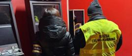 Funkcjonariusz Służby Celno-Skarbowej i funkcjonariuszka Policji stoją przed automatami do gier.