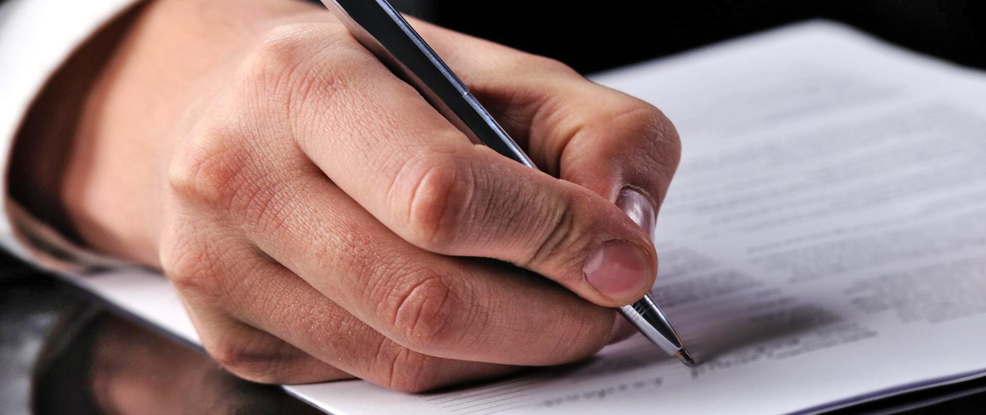 Baner przedstawiający dłoń trzymającą długopis.