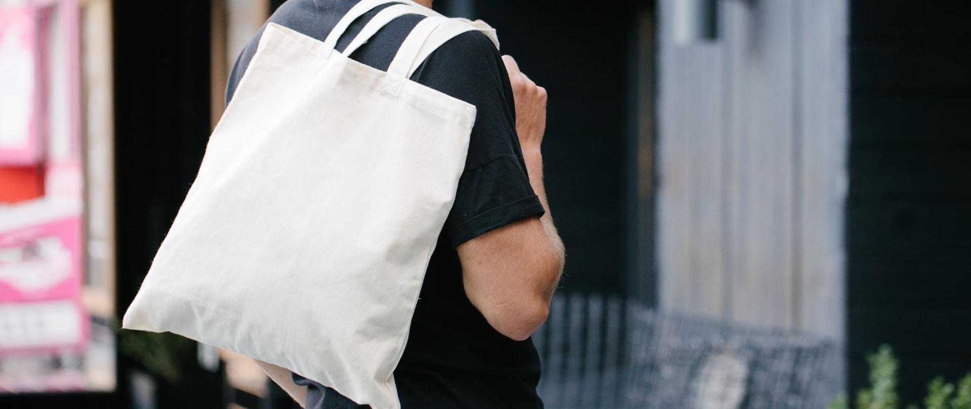 Mężczyzna niesie torbę materiałową, zarzuconą przez ramię, bez nadruków 