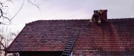 Strażak obok komina na dachu podczas gaszenia pożaru.