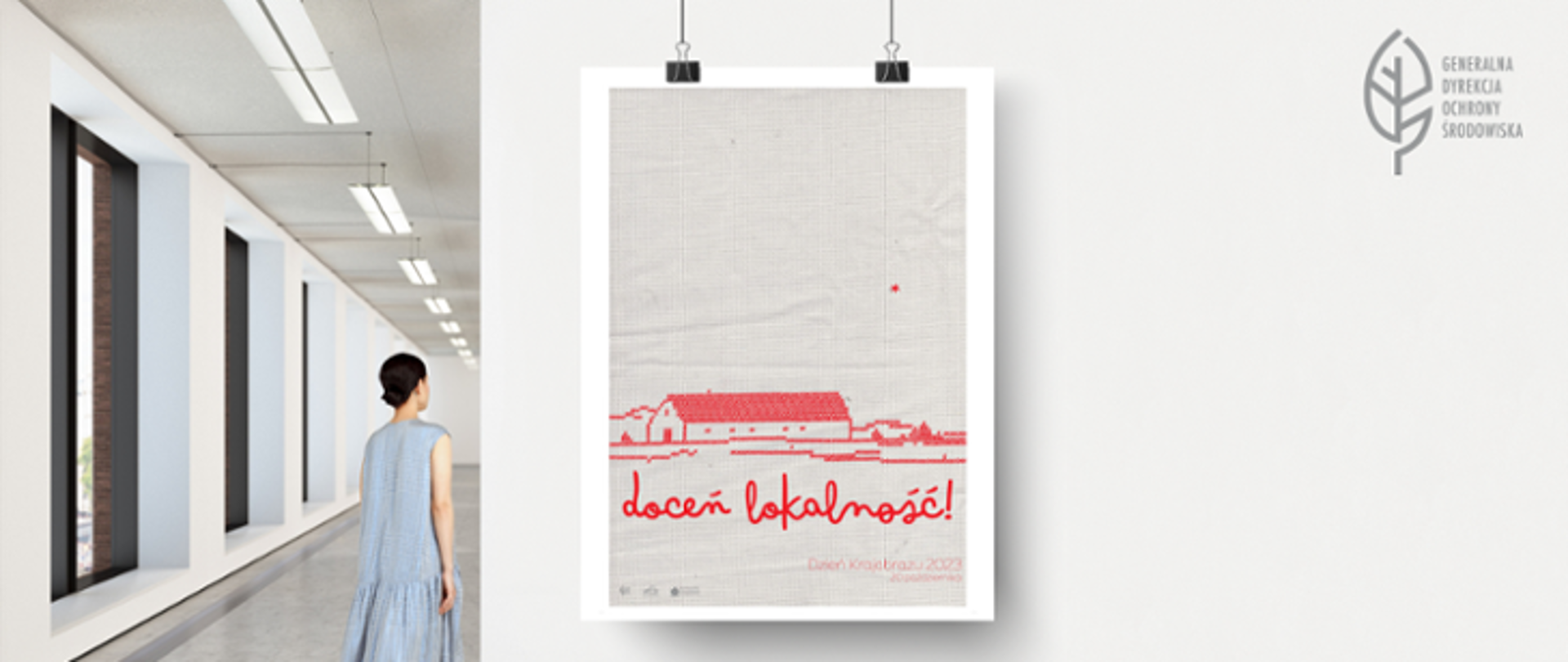 Galeria sztuki. Po lewej stronie stoi młoda kobieta w niebieskiej sukience. Przygląda się pracy zawieszonej na ścianie. Jest to plakat. Tło plakatu przypomina materiał wykorzystywany do haftu krzyżykowego. W dolnej części plakatu na czerwono jakby haftem krzyżykowym przedstawiony zarys prostokątnego budynku oraz również czerwonymi krzyżykami element krajobrazu. Poniżej napis w kolorze czerwonym: doceń lokalność. Niżej hasło: Dzień Krajobrazu 2023 - 20 października. W lewym dolnym rogu w kolorze szarym trzy logotypy: GDOŚ, Europejskiej Konwencji Krajobrazowej oraz NFOŚiGW.