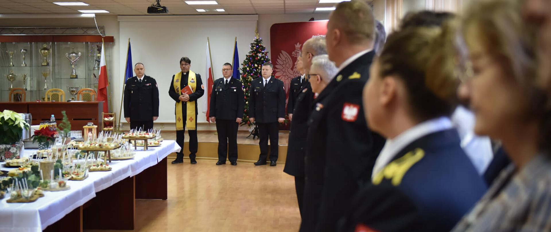 w oddali stoją komendanci wojewódzcy i kapelan po lewej stół zastawiony daniami, po prawej strażacy i pracownicy cywilni