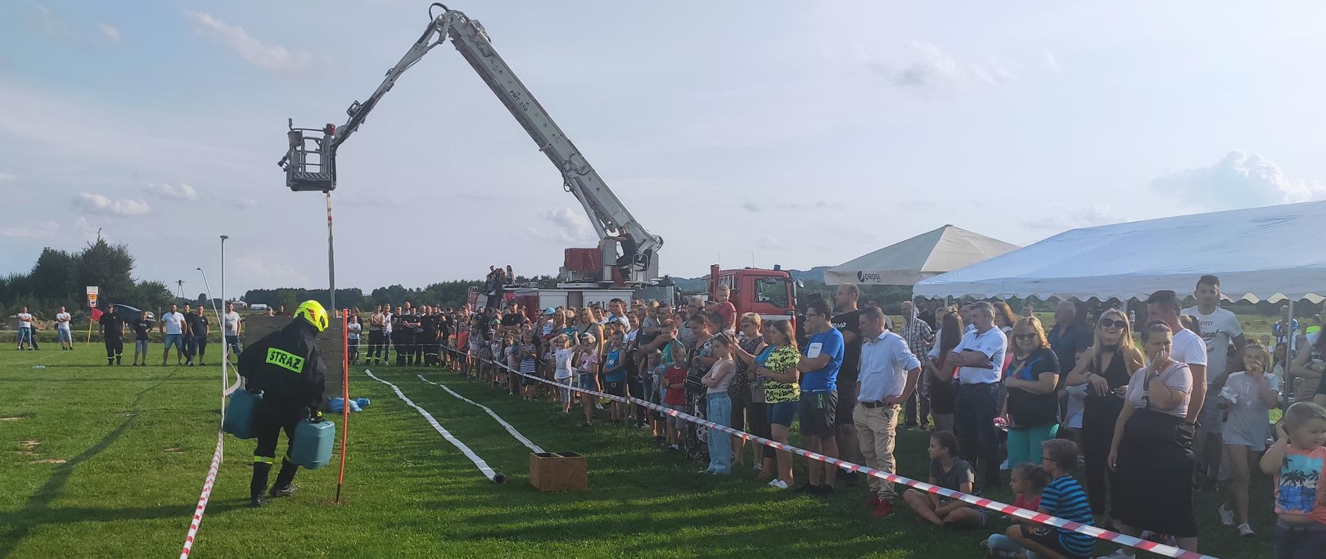 na zdjęciu tor przeszkód , strażak wykonuje ćwiczenie wokół zgromadzona widownia