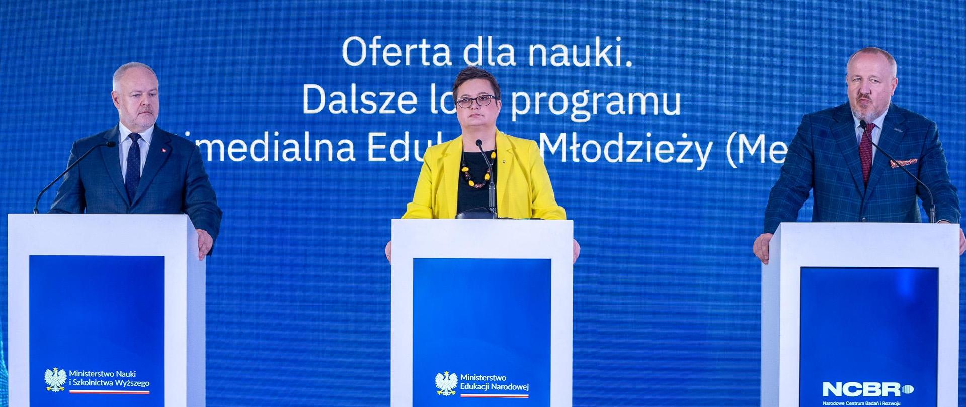 Na tle wbudowanego w ścianę wielkiego ekranu z napisem Oferta dla nauki. Dalsze losy programu Multimedialna Edukacja Młodzieży stoją przy trzech mównicach od lewej: wiceminister nauki i szkolnictwa wyższego Marek Gzik, wiceminister edukacji Katarzyna Lubnauer oraz Jerzy Małachowski dyrektor Narodowego Centrum Badań i Rozwoju 
