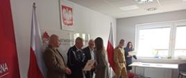 Zdjęcie przedstawia Komendanta Powiatowego PSP w Człuchowie, członków komisji egzaminacyjnej oraz sponsorów podczas wręczania nagród uczestnikom konkursu. W tle godło i flaga państwowa.
