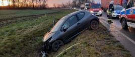ŚLISKI PORANEK. Na zdjęciu widać rozbity samochód osobowy, który znajduje się w rowie, obok stoją pojazdy służb ratowniczych i przejeżdżające samochody.