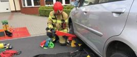 Strażak podczas doskonalenia zawodowego z ratownictwa technicznego umieszczający podbudowę z drewnianych klocków podczas podnoszenia samochodu osobowego przy użyciu poduszek pneumatycznych.