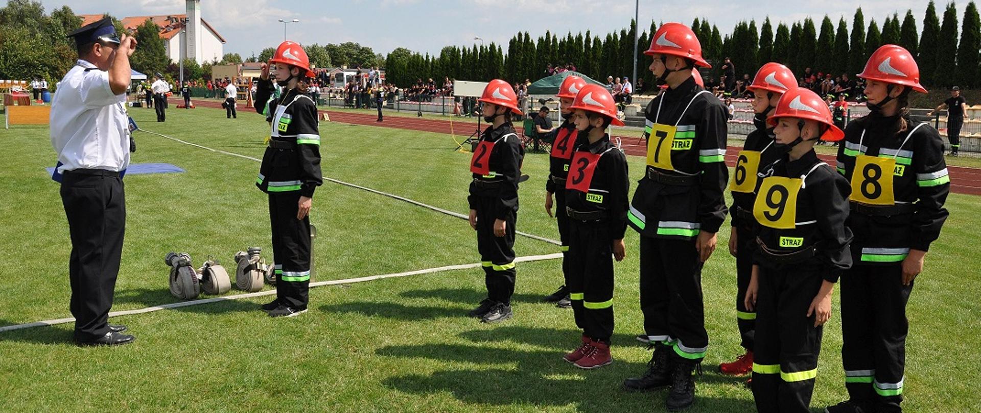 Na zdjęciu po lewej stronie sędzia zawodów przyjmujący meldunek od dowódcy młodzieżowej drużyny pożarniczej podczas wykonywania musztry