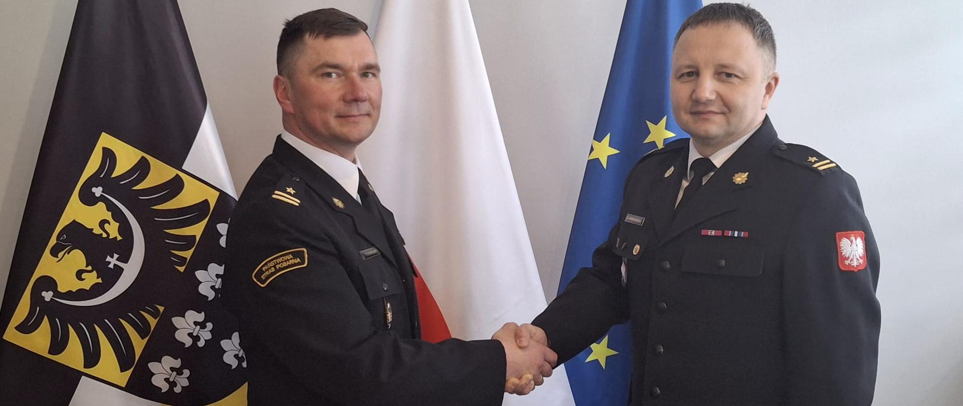 Strażacy w mundurach galowych podają sobie ręce. 