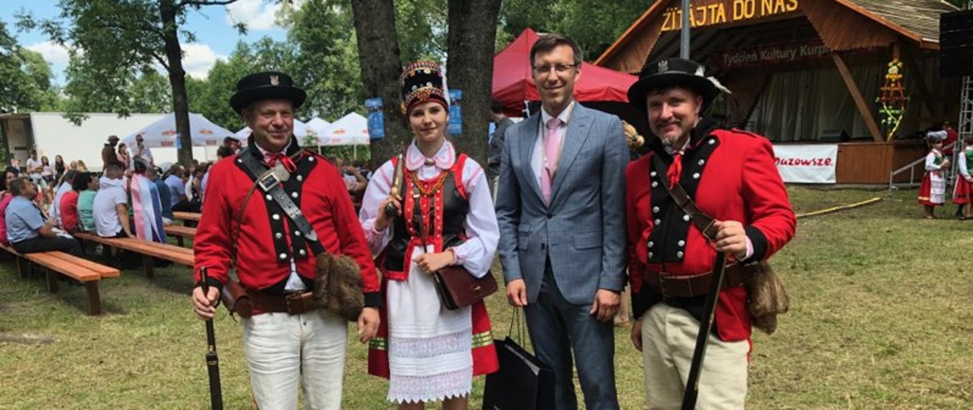 Na zdjęciu znajduje się trzech mężczyzn oraz jedna kobieta. Dwóch mężczyzn i kobieta ubrani są w stroje ludowe.