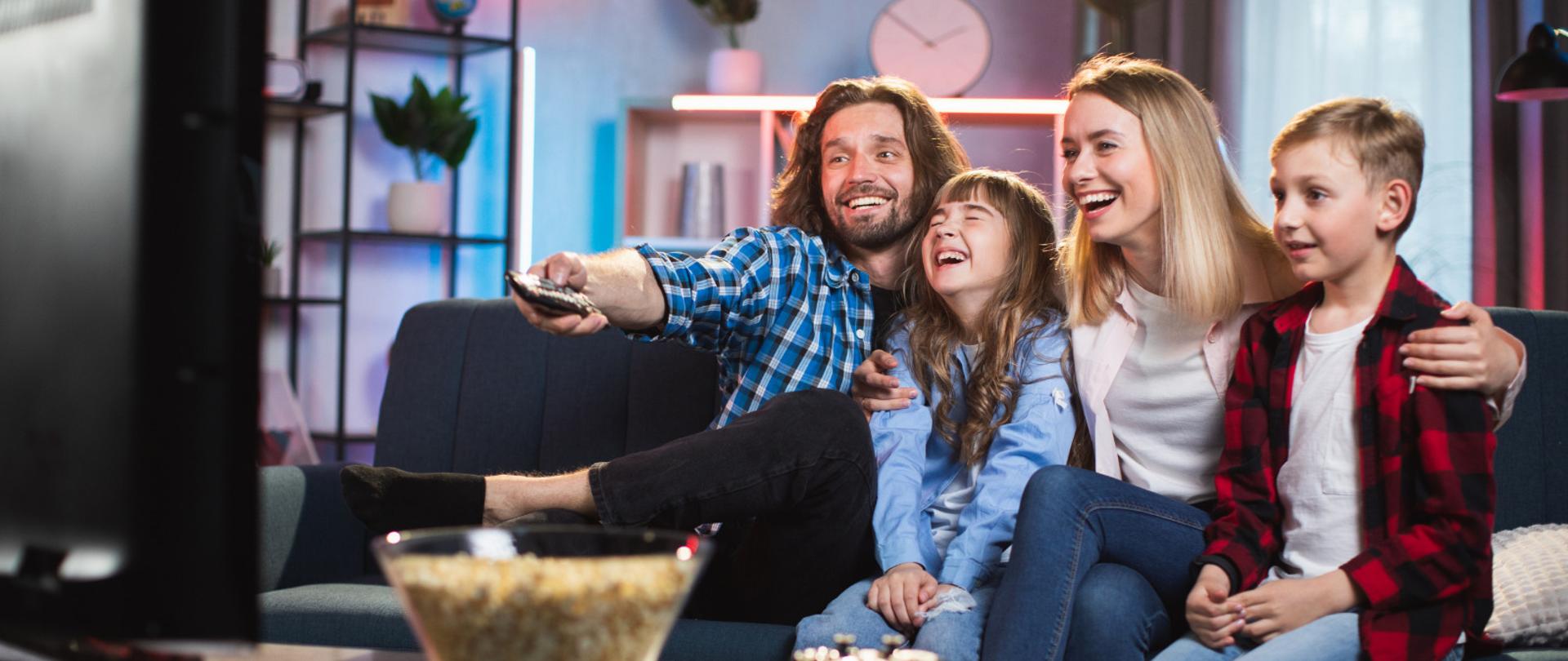 Młoda para z dziećmi na kanapie przed telewizorem