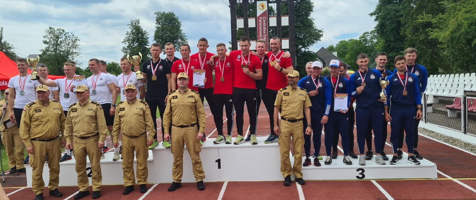 Na zdjęciu na podium stoją zwycięskie drużyny, przed nimi komendanci