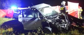 Wypadek na drodze wojewódzkiej nr 309. Zderzenie trzech pojazdów. Na pierwszym planie wrak forda, który ma bardzo mocno uszkodzony przód, za nim fragment toyoty. Koło samochodu stoi strażak. Teren zabezpieczony jest parawanem ochronnym.