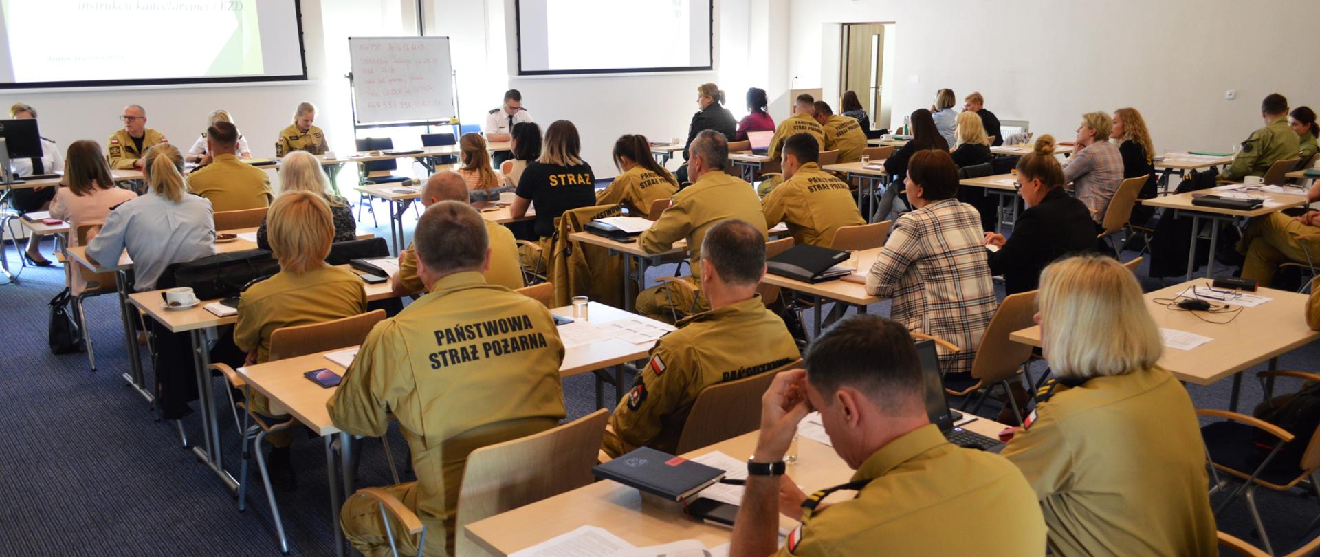 Na sali wykładowej w ławkach siedzą uczestnicy szkolenia (widok z tyłu), w umundurowaniu PSP oraz część osób w ubraniach cywilnych