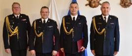 na zdjęciu czterech strażaków w umundurowaniu wyjściowym pozujących do zdjęcia na tle ściany za nimi stoją flagiapolski i unii europejskiej 