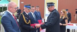 Zdjęcie przedstawia prezesa Ochotniczej Straży Pożarnej w Strużce, który wręcza upominki za zaangażowanie i pomoc przy pozyskaniu nowego samochodu.