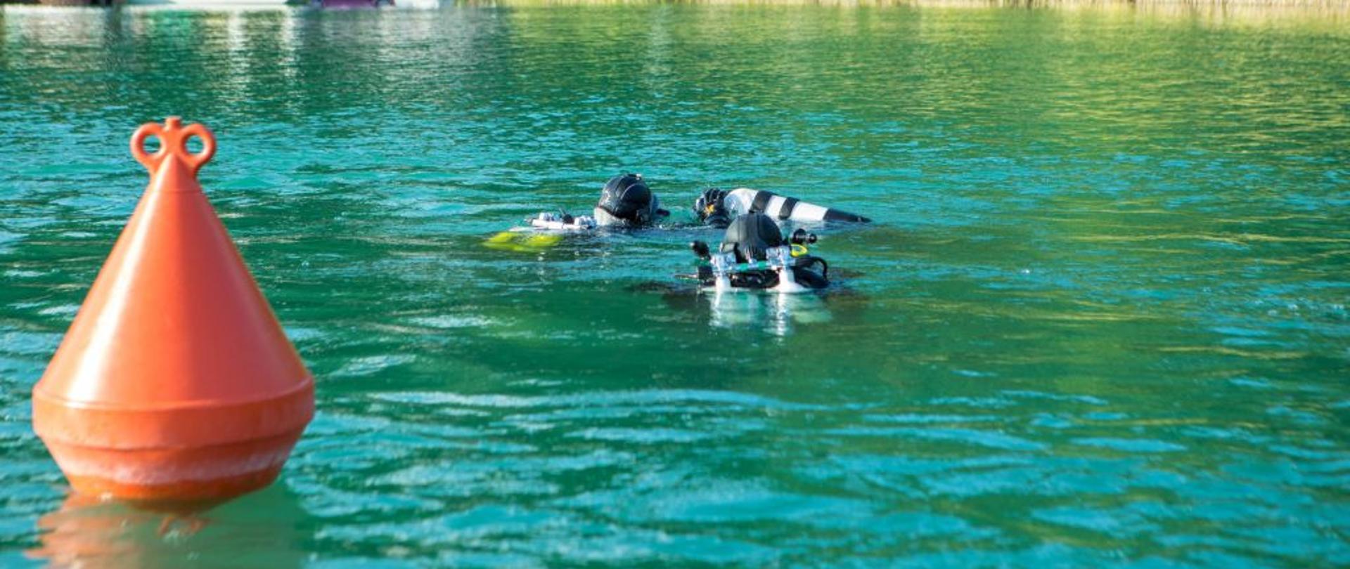 Dzień, słonecznie, bez opadów. Na zdjęciu widoczni są strażacy w trakcie ćwiczeń nad jeziorem. 