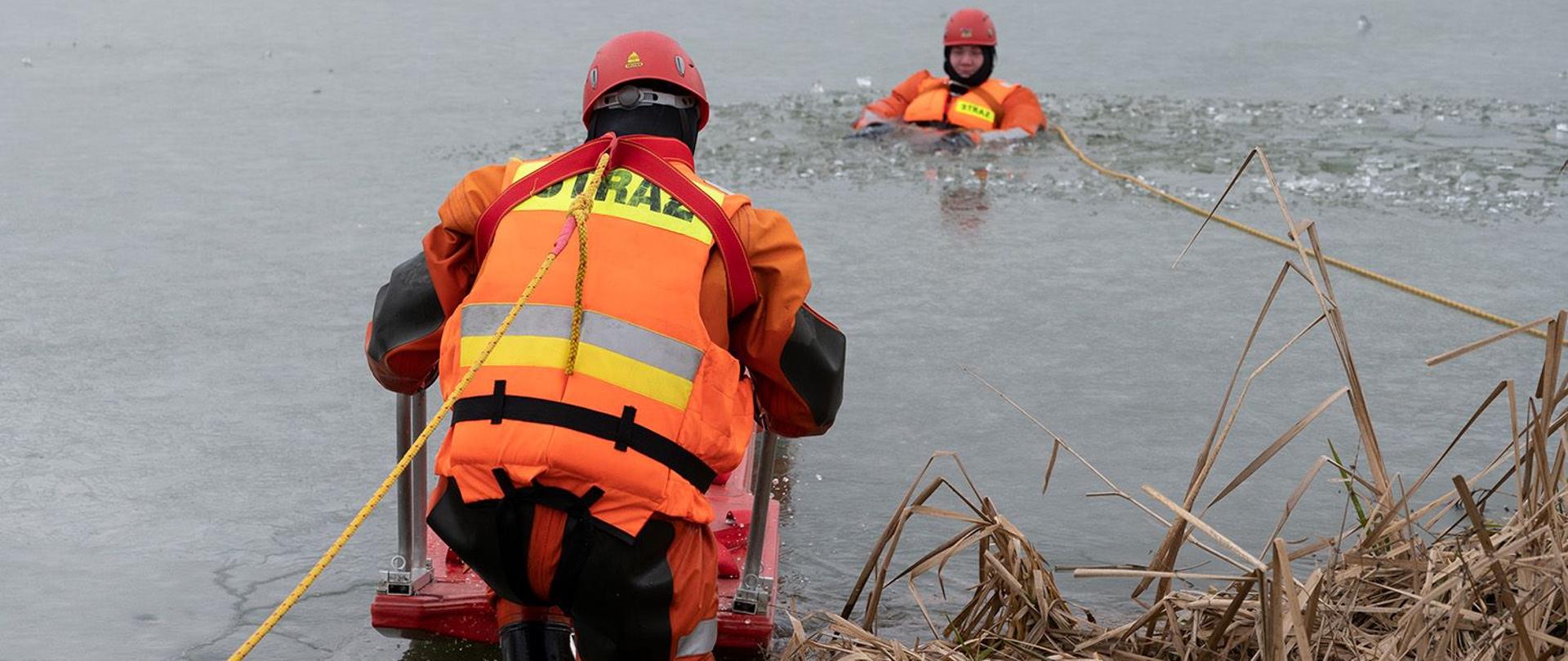 Na zdjęciu widoczni ratownik s saniami lodowymi ratujący poszkodowanego z przerębla lodowego