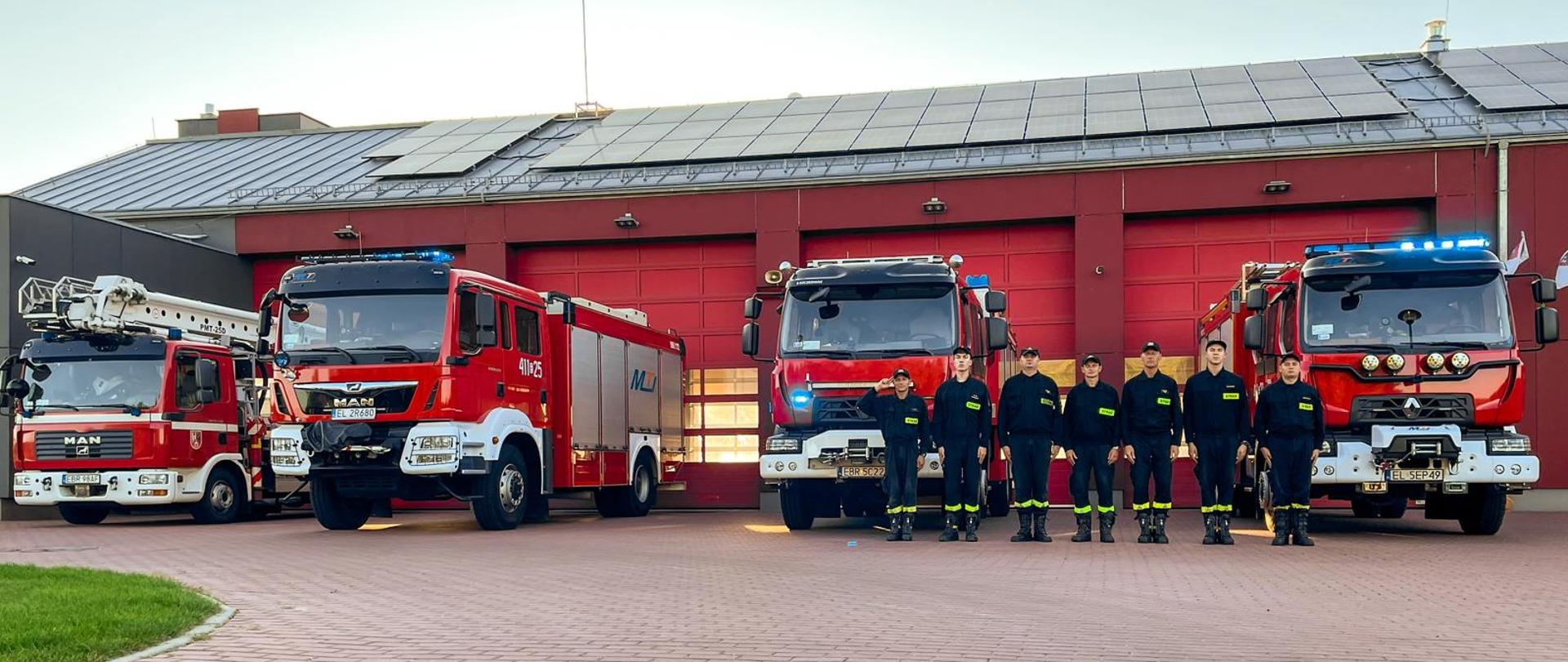 na placu komendy powiatowej psp w brzezinach strażacy ustawieni w szeregu oddają hołd zmarłym tragicznie strażakom osp żukowo na tle komendy oraz samochodów bojowych cała zmiana oddaje honor salutując