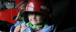 Zdjęcie przedstawia uśmiechnięte małe dziecko w strażakim hełmie w samochodzie gaśniczym
