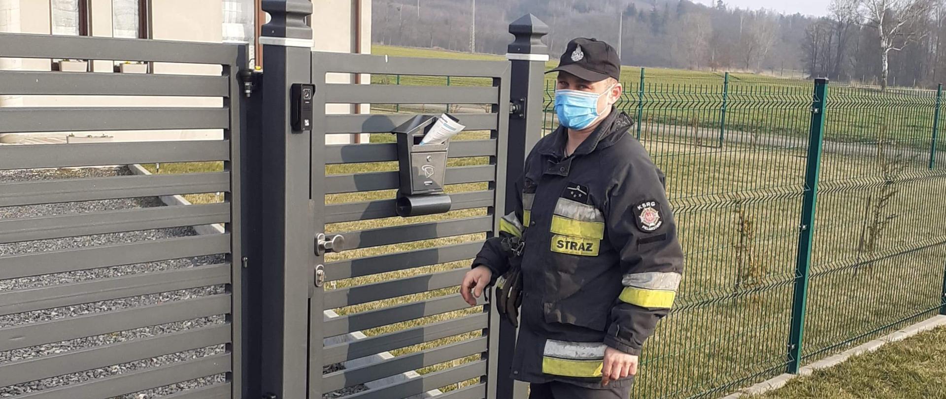 umundurowany strażak wkładający ulotkę informacyjną do skrzynki na listy w budynku jednorodzinnym