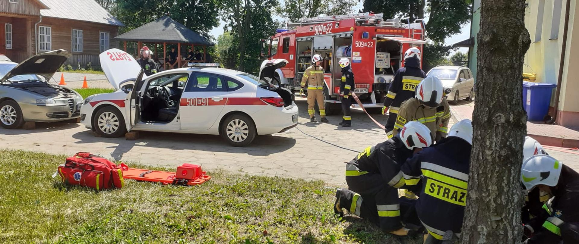 Strażacy udzielają pomocy poszkodowanemu w wyniku kolizji dwóch samochodów osobowych.