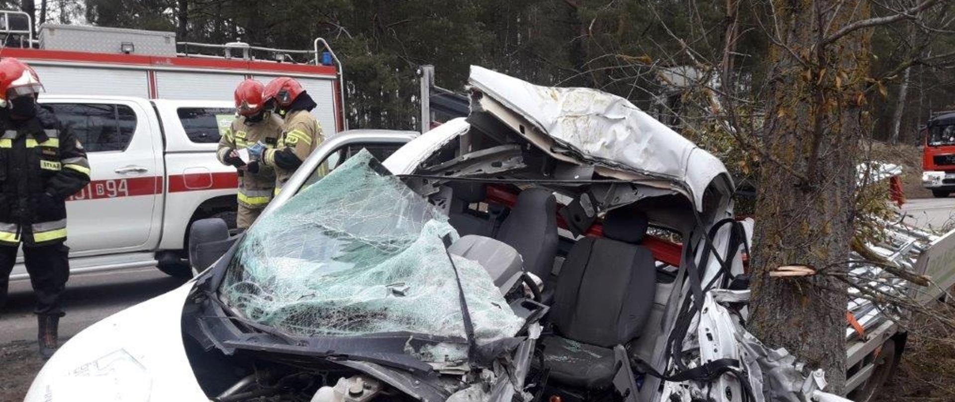 Zniszczony w wypadku samochód dostawczy. W tle strażacy PSP i pojazdy pożarnicze.