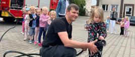 Dziecko pod nadzorem strażaka podaje prąd wody