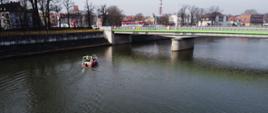 Zdjęcie wykonane z drona. Fotografia przedstawia łódź straży pożarnej płynąca Odrą przy moście w Kędzierzynie-Koźlu.