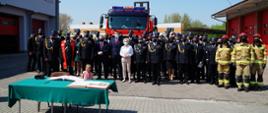 Zdjęcie przedstawia Powiatowe Obchody Dnia Strażaka w Białogardzie. Zdjęcie zbiorowe uczestników obchodów na tle samochodu strażackiego