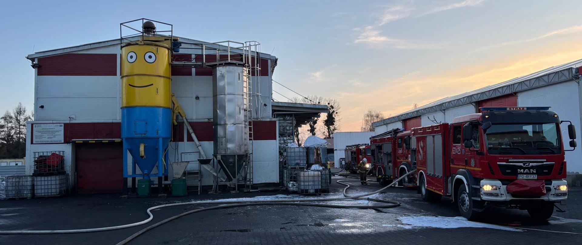 Strażacy gaszą pożar hali produkcyjnej, która praktycznie na zdjęciu jest już spalona. Widać spalone elementy i zawalającą się halę produkcyjną.