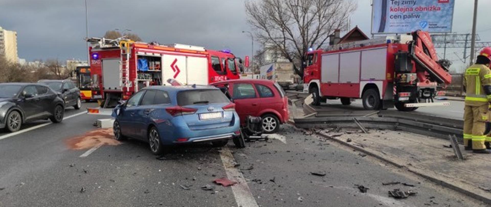 Na zdjęciu znajdują się dwa rozbite samochody osobowe pokazane od tyłu. W tle dwa samochody strażackie.