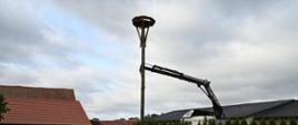 Dźwig ustawiający platformę pod gniazdo bocianie. Wokół zabudowania jednorodzinne. 