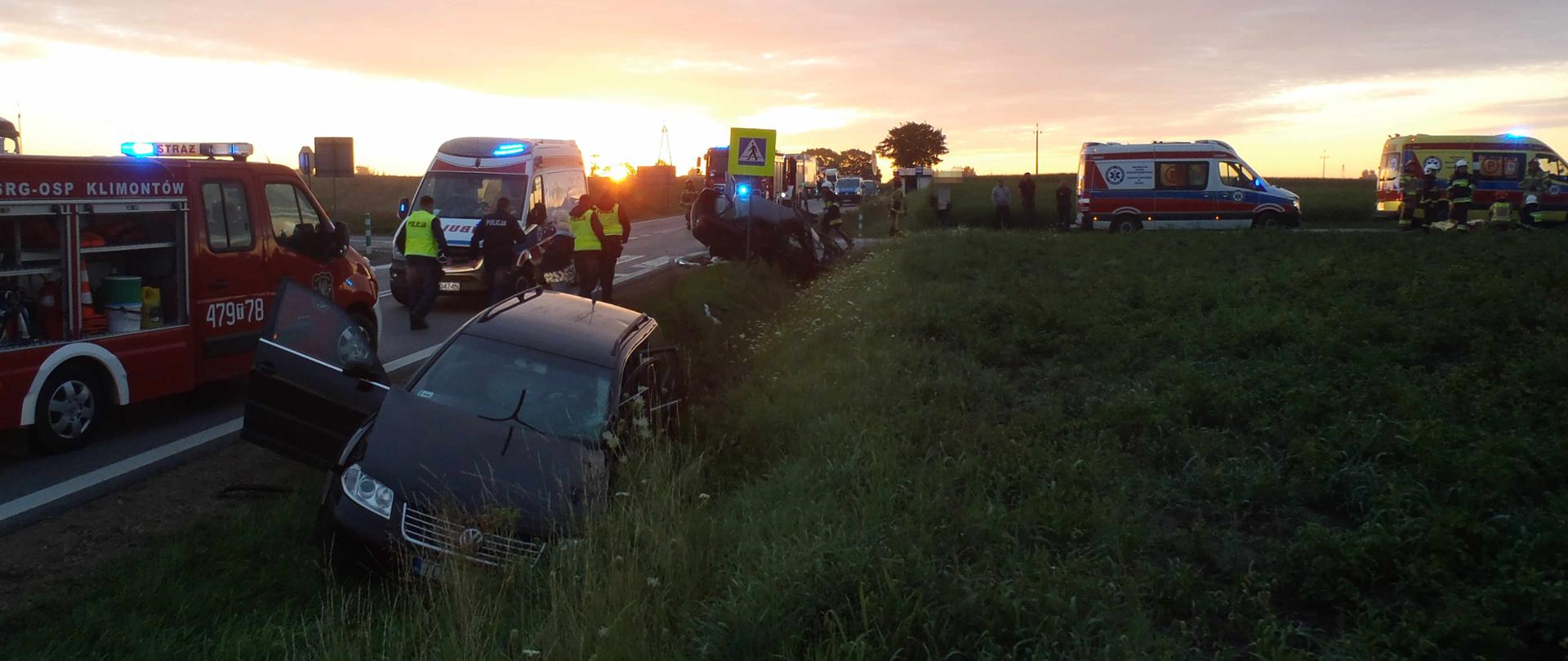 Na pierwszym planie w rowie znajduje się jeden z uszkodzonych pojazdów. Po lewej na drodze głównej stoi samochód strażacki i karetka, potem drugi z uszkodzonych pojazdów. Po lewej dwie karetki. W oddali stoją kolejne karetki i samochody strażackie. Po lewej wzdłuż samochód idzie czterech policjantów, a przy karetkach po prawej stoją strażacy.