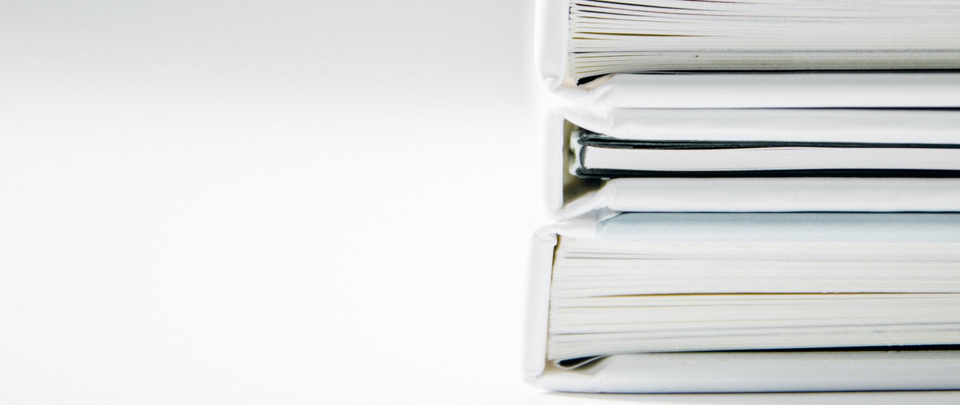 fragment trzech książek oprawionych w białe okładki ułożonych jedna na drugiej na białym tle