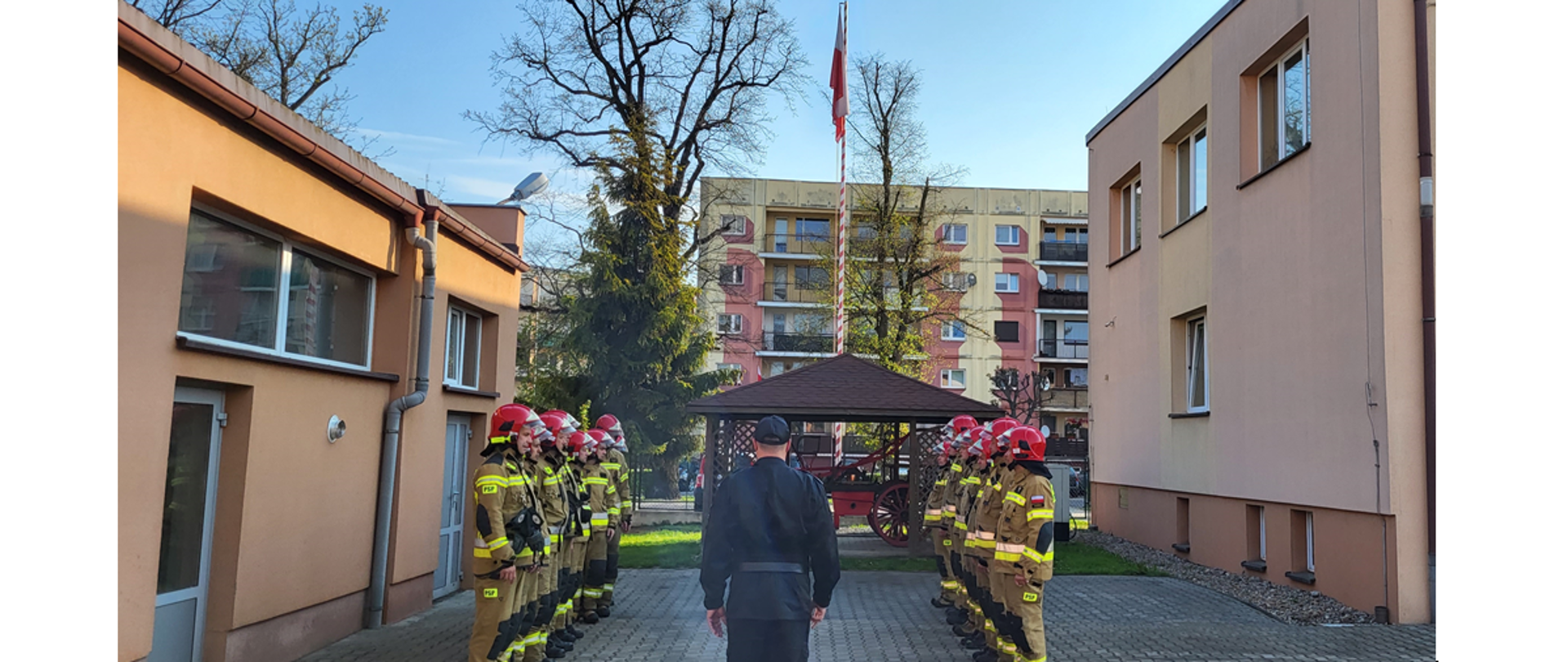 Na zdjęciu widać strażaków w trakcie uroczystej zmiany służby, w czasie której dokonano podniesienia flagi państwowej oraz odtworzeniem hymnu państwowego. 