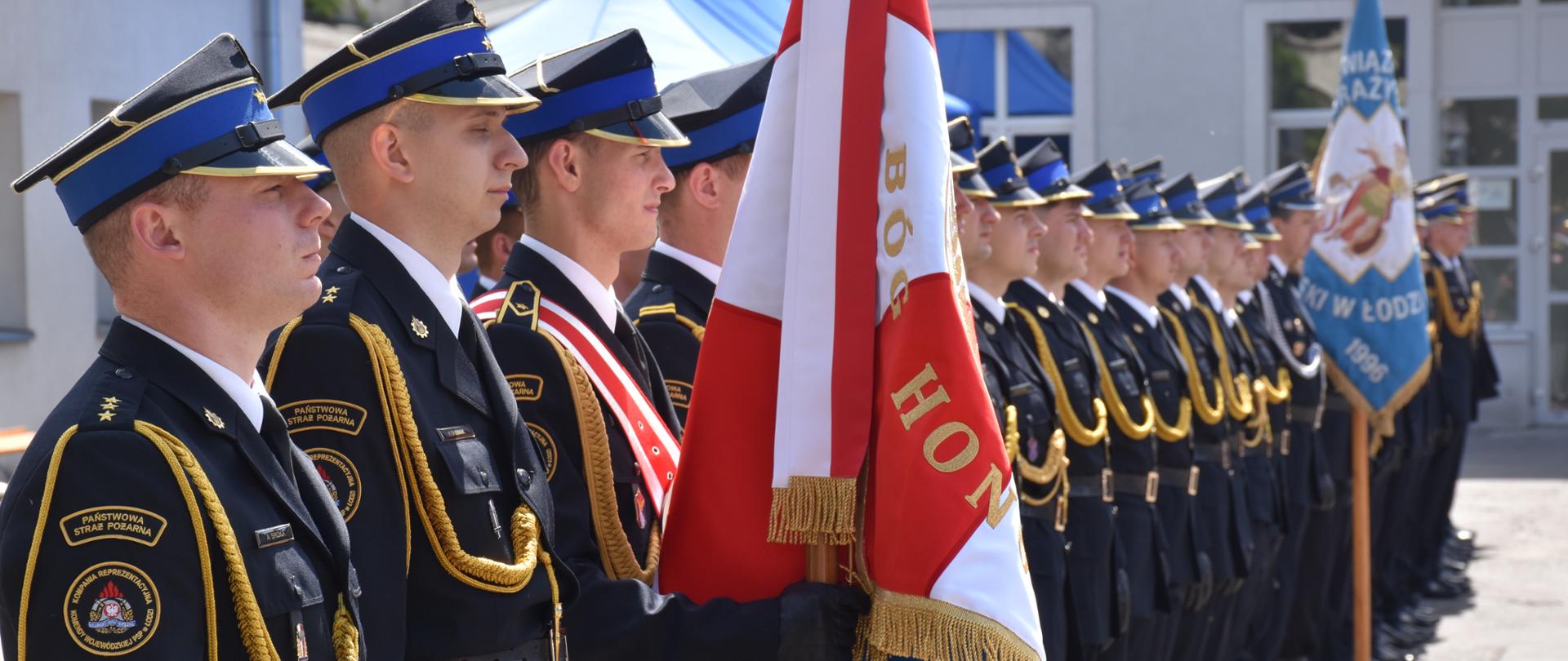 Poczet sztandarowy i funkcjonariusze PSP stojący w szyku podczas obchodów strażackiej uroczystości.