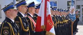 Poczet sztandarowy i funkcjonariusze PSP stojący w szyku podczas obchodów strażackiej uroczystości.