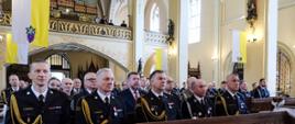 Strażacy i komendanci w pierwszych ławkach w kościele podczas uroczystej mszy z okazji dnia strażaka