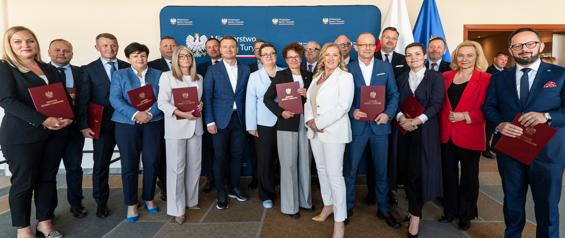 Minister Sportu i Turystyki, Sławomir Nitras z członkami Rady Polskiej Organizacji Turystycznej IX Kadencji. Za ich plecami ścianka z logotypami MSiT. Z prawej strony ścianki flagi Polski i UE.