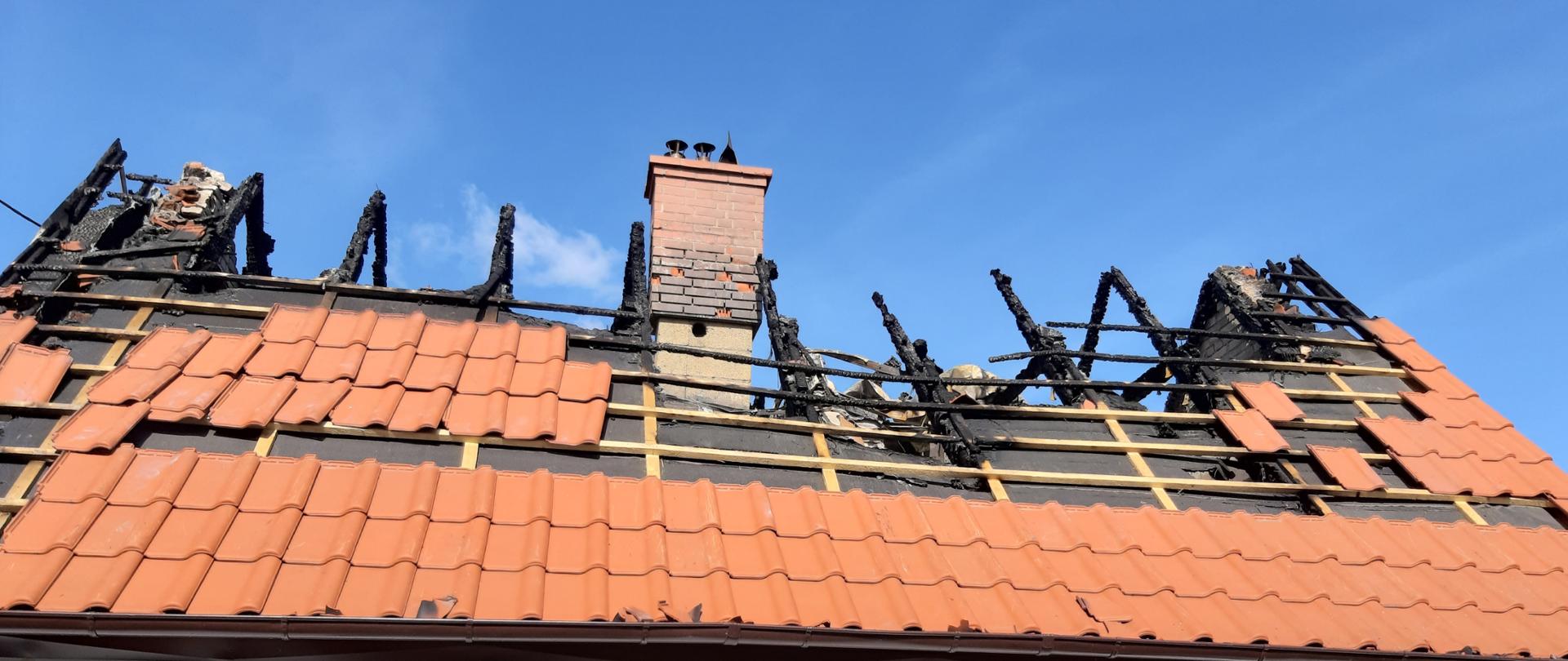 Budynek murowany z częściowo spalonym dachem. Budynek jednorodzinny jest koloru białego z brązowymi oknami a na dachu znajduje się czerwona dachówka. 