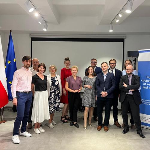 12 osób w oficjalnych strojach pozuje do zdjęcia z flagami Mołdawii Polski i UE w tle