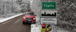 Widoczny samochód strażacki i strażak montujący tablice, pora zimowa. 