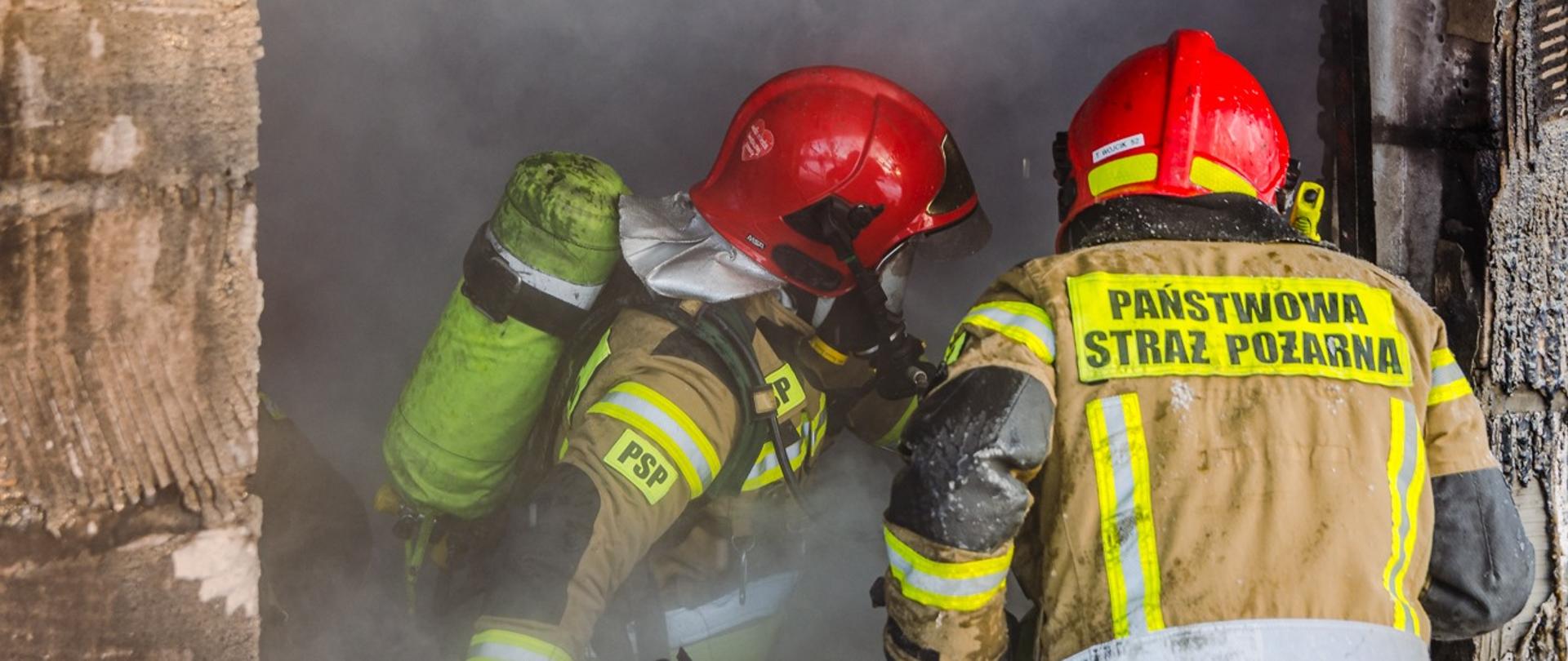 Zdjęcie przedstawia dwóch strażaków dogaszających altankę