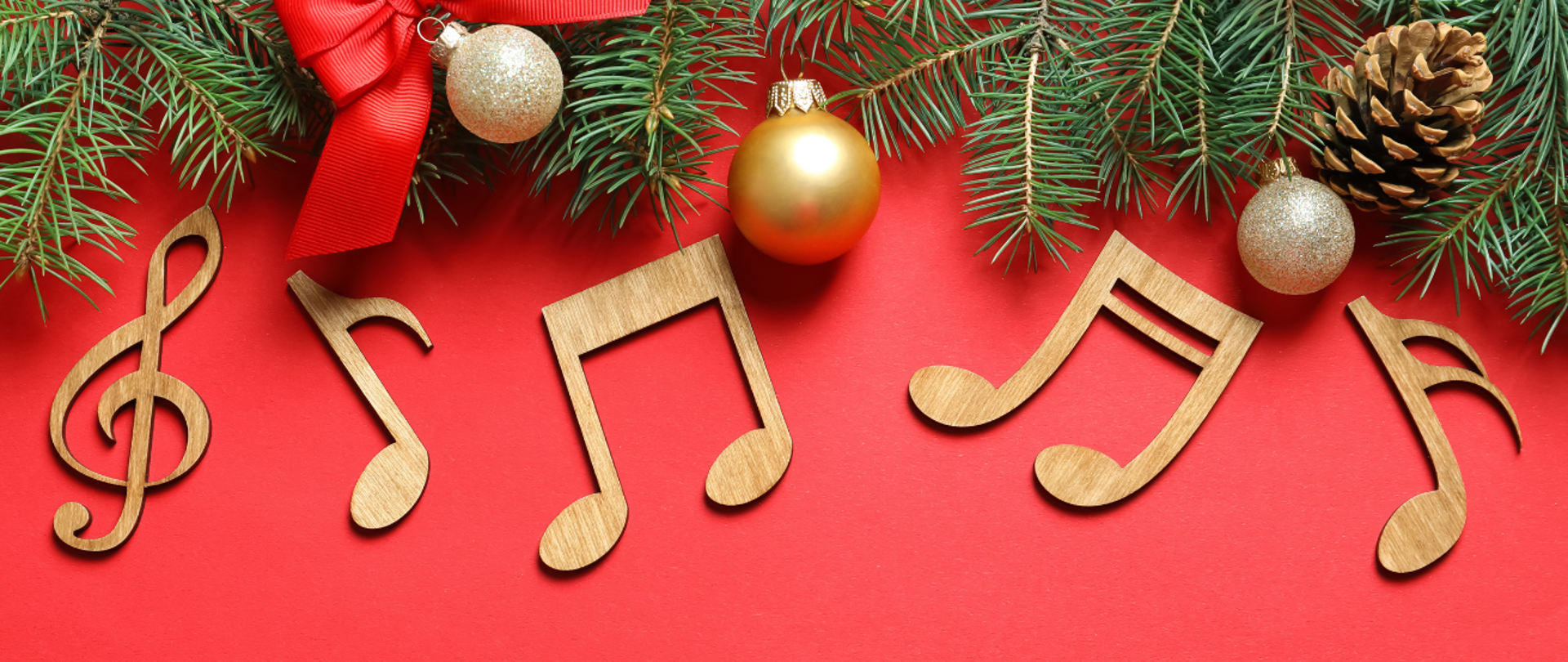 Zdjęcie przedstawia świąteczną kompozycję z zielonymi gałązkami jodły, czerwoną kokardą, bombkami (złotymi i srebrnymi) oraz drewnianymi nutami muzycznymi na jaskrawoczerwonym tle.