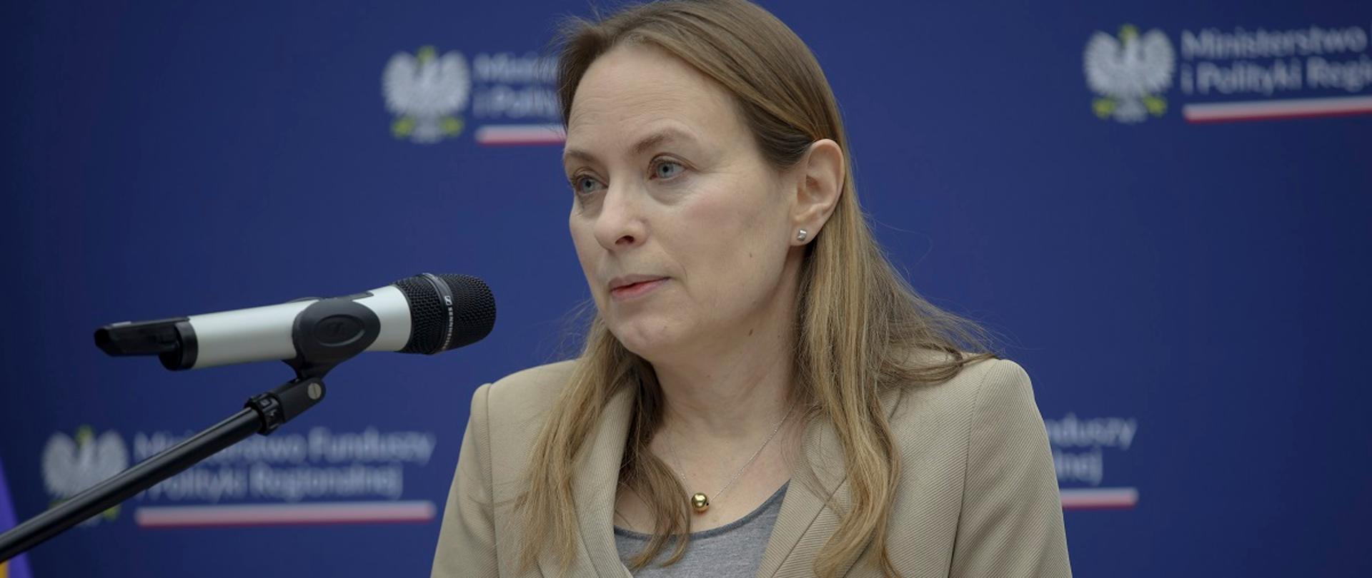  Minister funduszy i polityki regionalnej Katarzyna Pełczyńska-Nałęcz stoi przy mikrofonie, za jej plecami ścianka z logo MFiPR