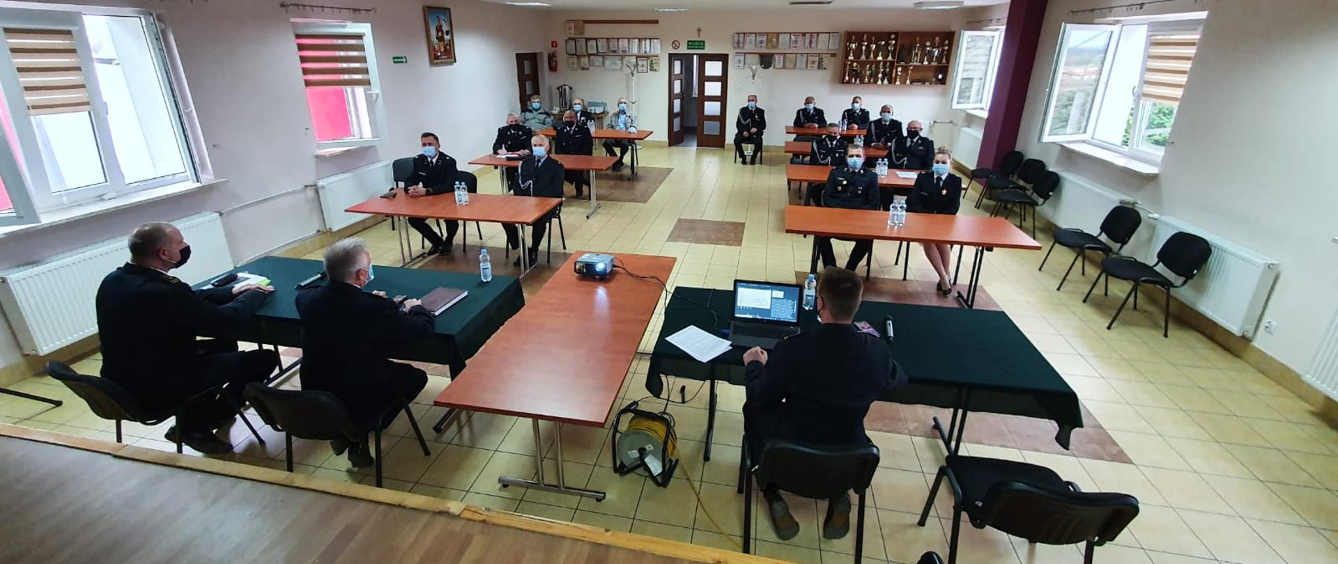 Na zdjęciu widnieje Zastępca Świętokrzyskiego Komendanta Wojewódzkiego PSP w Kielcach - st. bryg. Jarosław Piotrowski, Komendant Powiatowy PSP w Jędrzejowie - st. bryg. Paweł Jakubowski, Zastępca Komendanta Powiatowego PSP w Jędrzejowie - bryg. Tomasz Szymański oraz druhowie z terenu powiatu jędrzejowskiego. Wszyscy strażacy w umundurowaniu galowym. Zdjęcie zrobione na sali konferencyjnej OSP Prząsław. panowie dyskutują nad projektem ustawy o OSP.