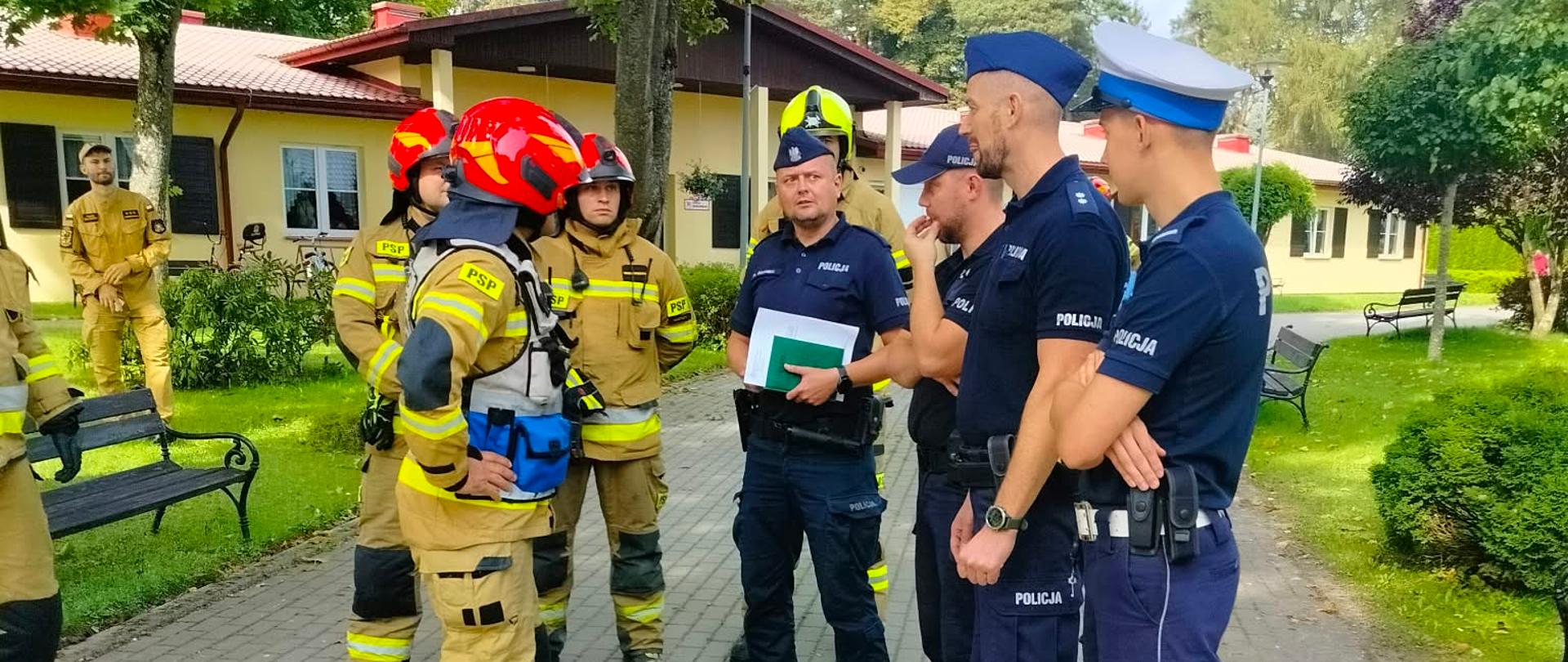 Na zdjęciu widać strażaków z policjantami naradzającymi się podczas ćwiczeń